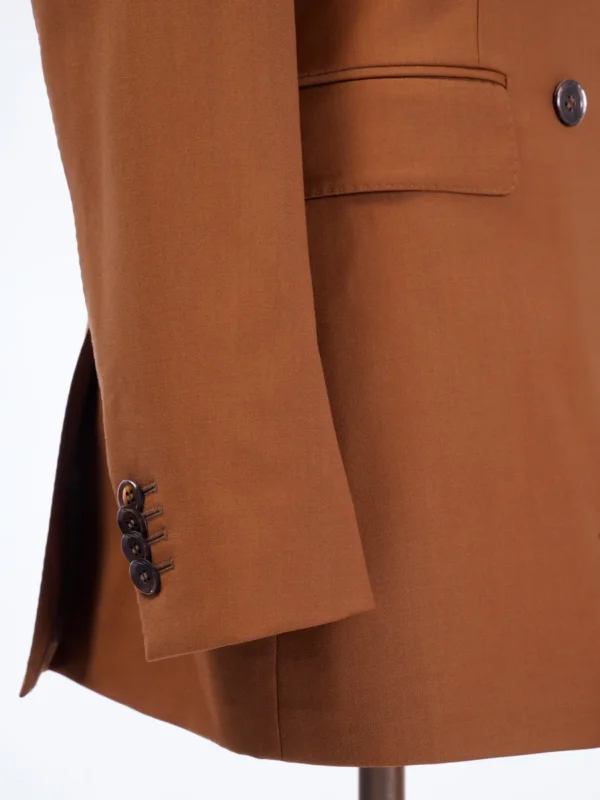 A close up of the sleeve and button on a brown jacket.